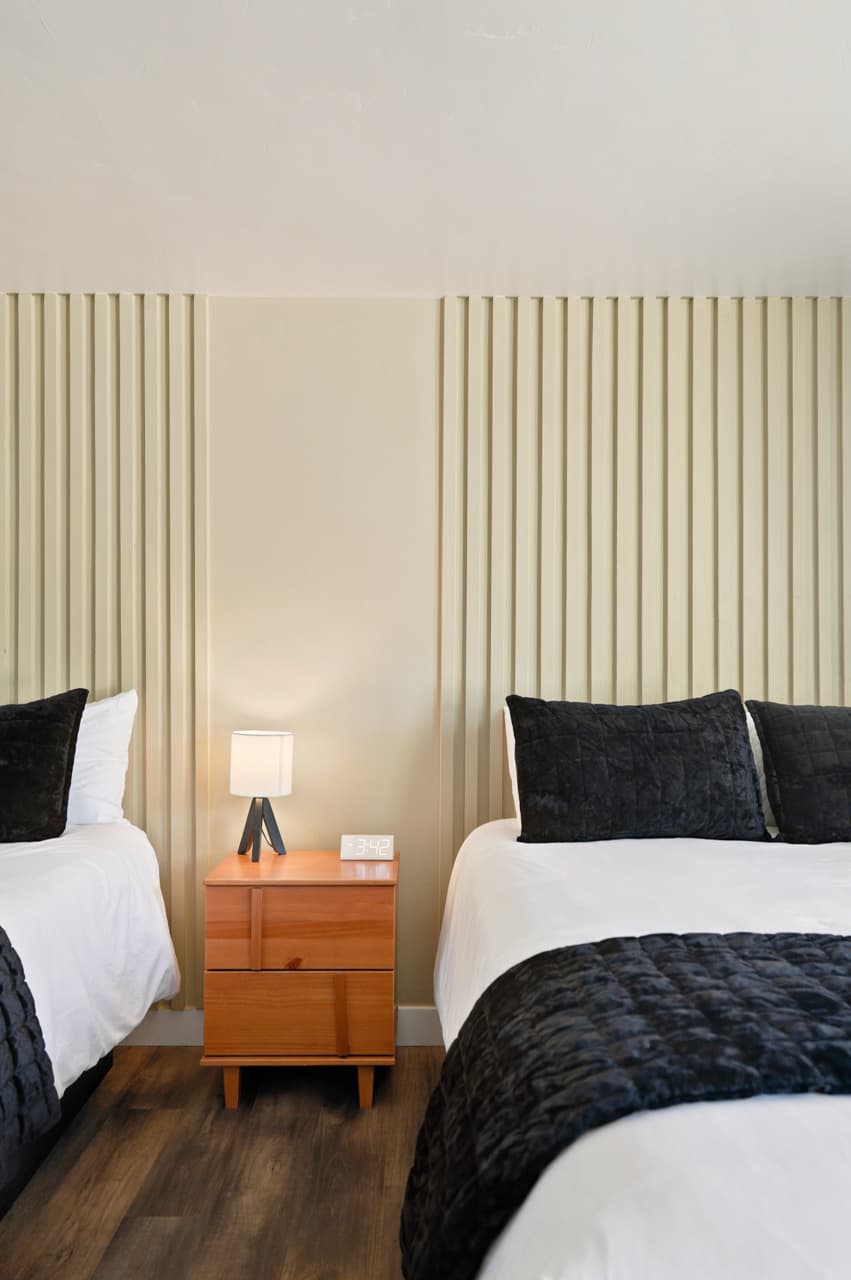 Two beds with black bedding and a nightstand in a remodeled room at Birch Glen Lodge